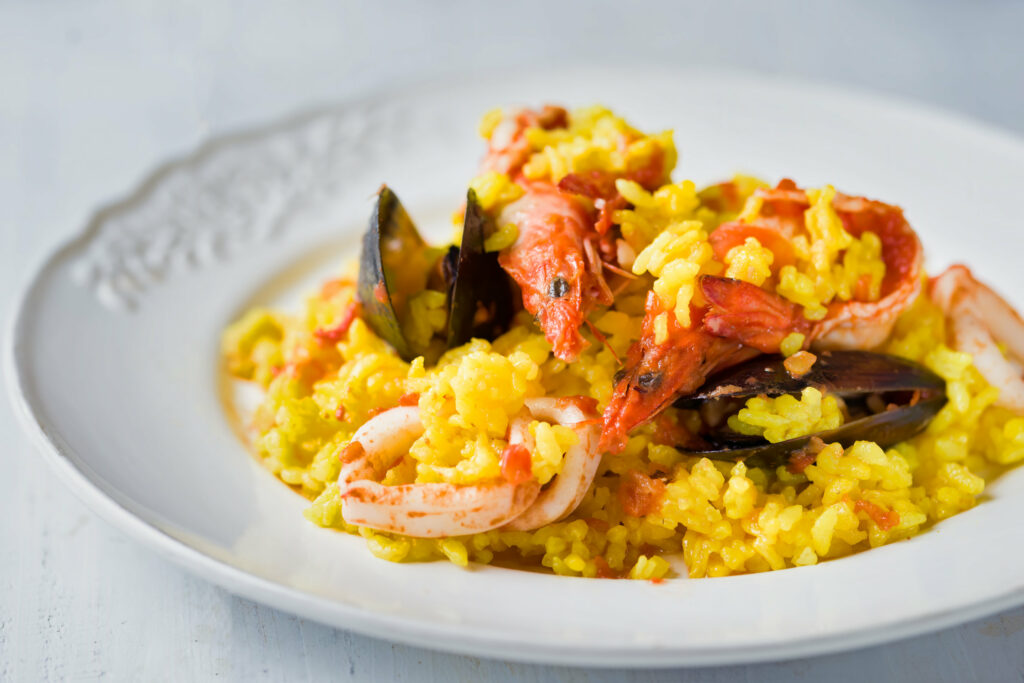 A plate of Spanish seafood paella with shrimp and mussels on a white surface.