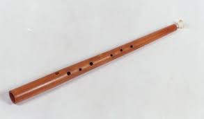 A wooden flute with six finger holes and a mouthpiece, lying against a white background.