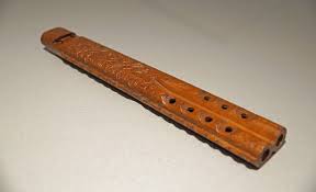 A wooden flute with intricate carvings lying on a plain surface.