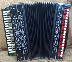 A black piano accordion with floral designs, white keys, red bass buttons, against a beige background.