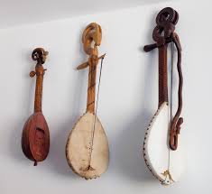 Three traditional stringed musical instruments hanging on a white wall.