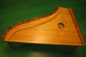 A wooden stringed instrument with a triangular body and a series of tuning pegs along one side, displayed on a green background.