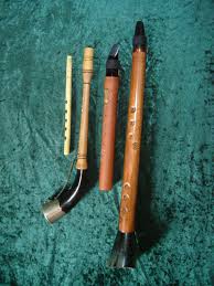 Three traditional Japanese bamboo flutes, known as shakuhachi, of varying lengths and designs, displayed on a textured green background.