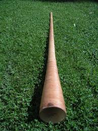 A long wooden didgeridoo lying on a grassy surface.