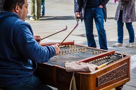 A person playing a large stringed instrument on a busy street, with pedestrians in the background.