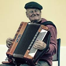 An elderly man wearing a beret playing an accordion and smiling.