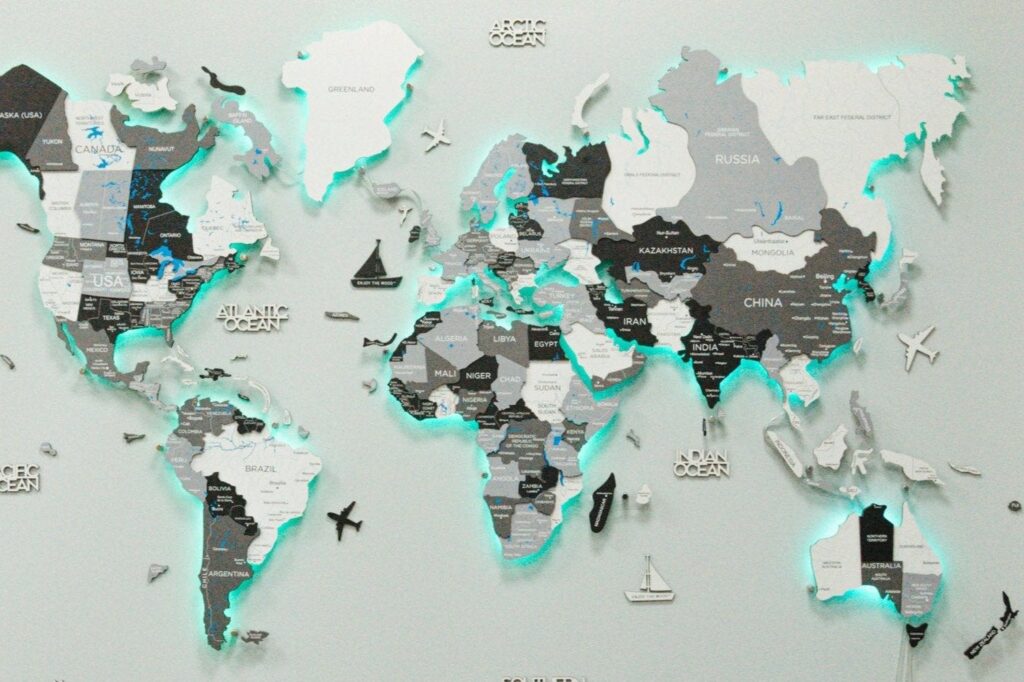 A 3D wooden world map wall art in blue and grey, with white-highlighted countries and decorative airplanes and ships.