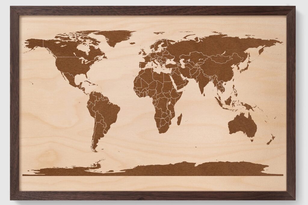 A framed world map with a simplistic design, featuring continents in a dark color on a light wooden background.