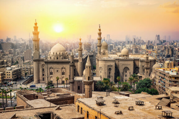 Sunset view over Cairo, Egypt, highlighting the city's architecture with mosques and minarets against a hazy sky.