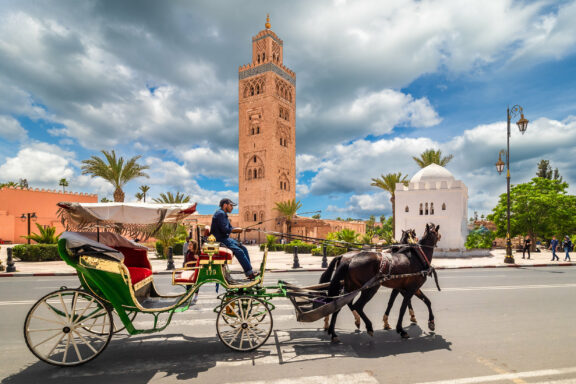 A horse-drawn carriage and driver in Marrakesh, Morocco, with the Koutoubia Mosque's tall minaret in the background.