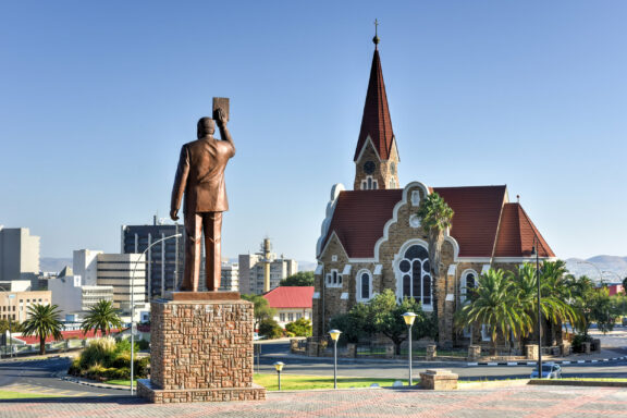 A statue overlooks a steepled church in Windhoek, Namibia, with modern buildings in the background under a clear sky.