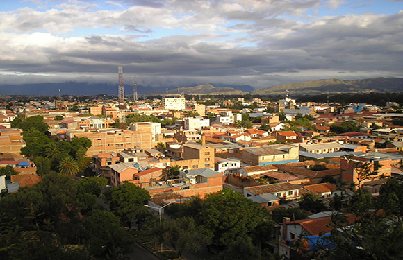 A panoramic view of Tarija, a city in Bolivia, with buildings under a cloudy sky at dusk.