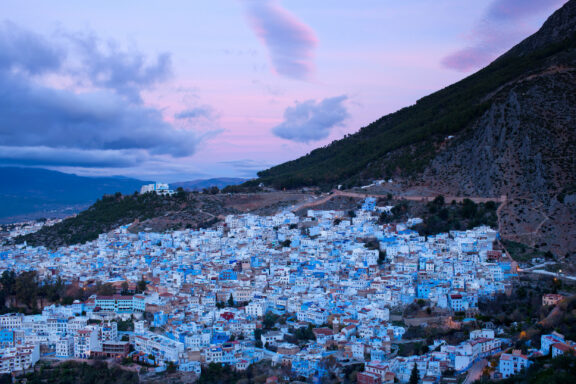 Twilight view of Chefchaouen, Morocco, featuring its unique blue houses against a mountain and colorful sky.