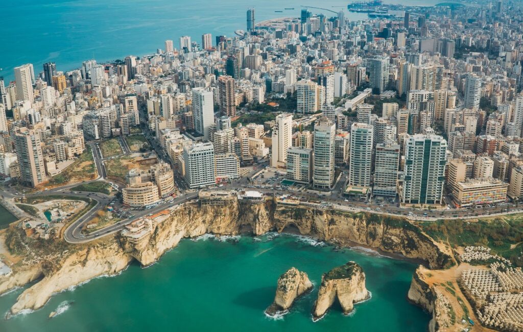 Aerial view of a densely built coastal city with high-rise buildings near a cliff and a body of water, possibly Beirut.