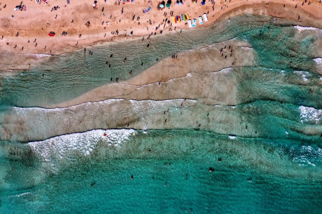 Aerial view of a beach with clear turquoise waters, sandy shore, and people scattered around the beach area.