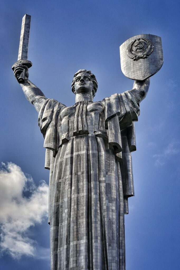 A statue in Kyiv, Ukraine, shows a female figure with a sword and shield against a blue sky.