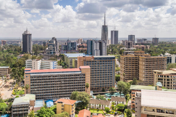 Aerial view of Nairobi, Kenya, showcasing a mix of modern high-rise buildings and lush greenery under a cloudy sky.