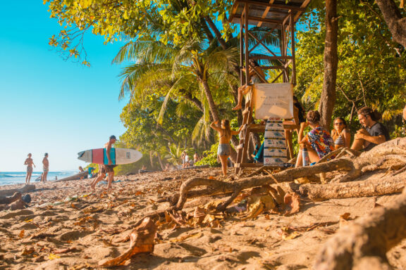 People are enjoying a sunny day on Santa Teresa beach, Costa Rica, with palm trees and blue skies.