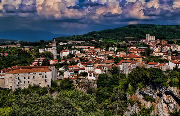 Aerial view of Pazin, a town in Croatia, showcasing historic buildings, red-tiled roofs, and surrounding greenery under a cloudy sky.