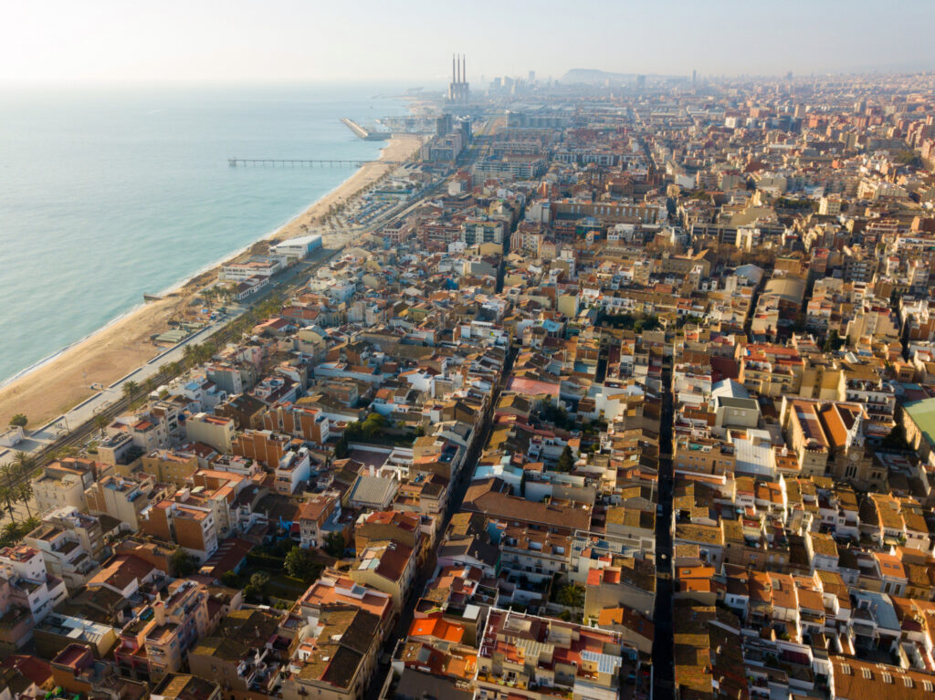 Aerial view of Badalona, Spain shows a dense urban landscape, closely packed buildings, streets, and a Mediterranean beachfront.