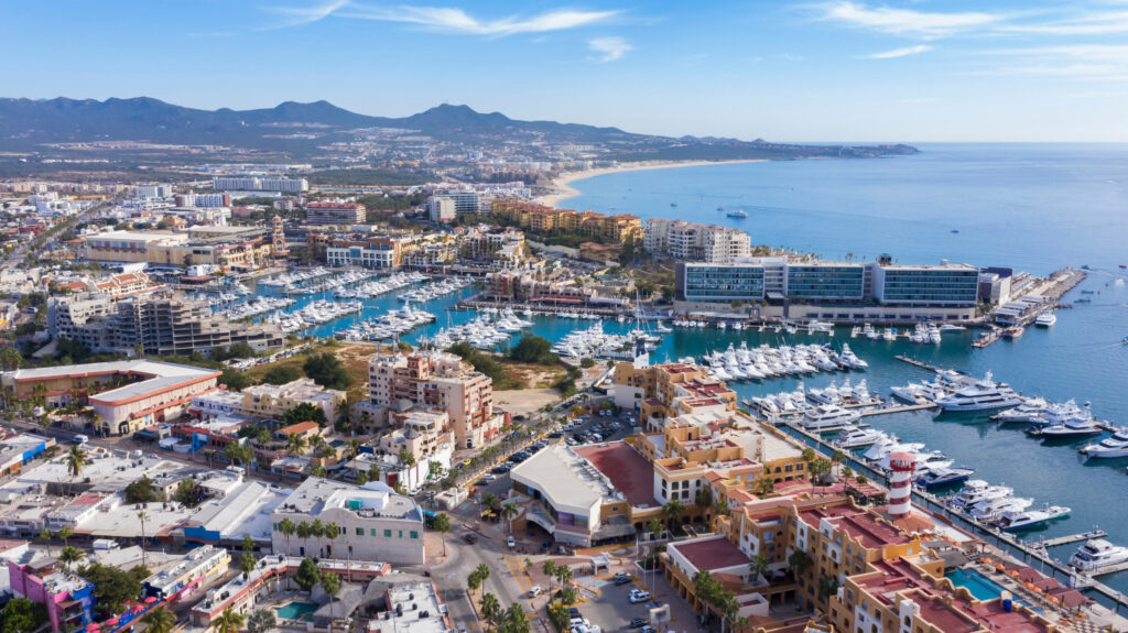 Aerial view of a coastal city with marina, dense buildings, and a long beach in Baja California Sur.