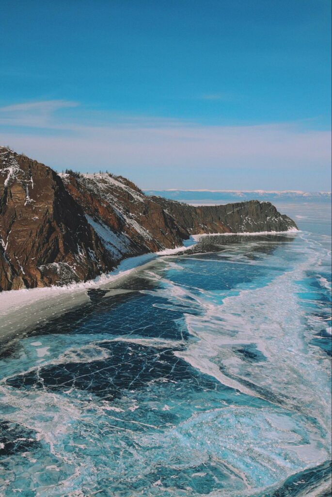 A vertical image depicts a frozen, rugged Russian coastline with cliffs, ice, open water, and snow under a clear sky.