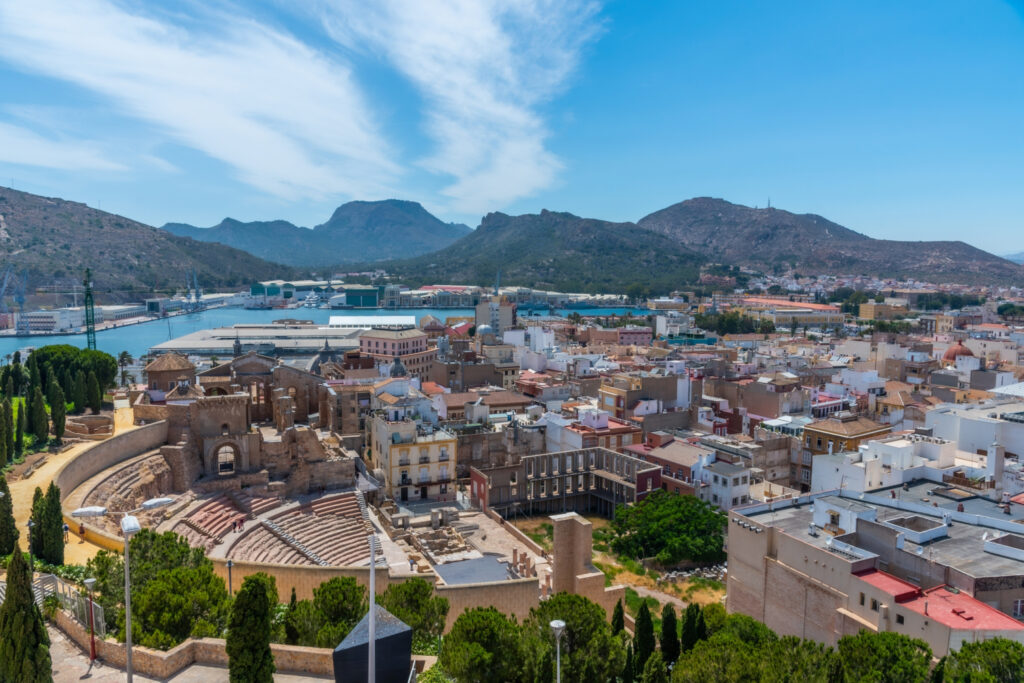 Aerial view of Cartagena, Spain, showcasing the cityscape with historic buildings and the surrounding hills under a clear blue sky.