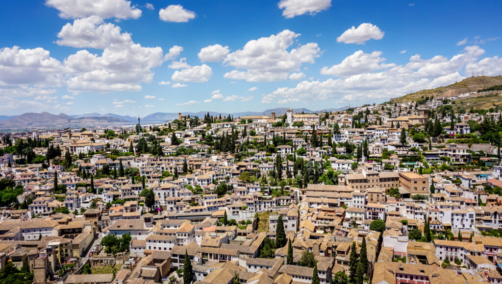 A panoramic view of Granada with traditional buildings and greenery under a partly cloudy sky.