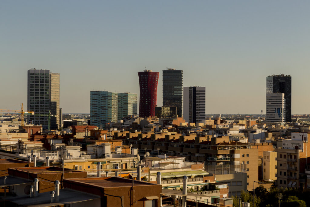 A cityscape of L'Hospitalet de Llobregat with a mix of modern high-rise buildings and traditional low-rise structures under a clear sky.