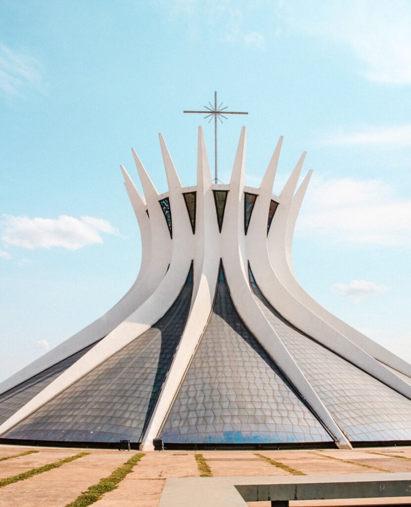 A photo shows the Cathedral of Brasília, a modernist building with a crown-like shape and curved columns, under a clear blue sky.