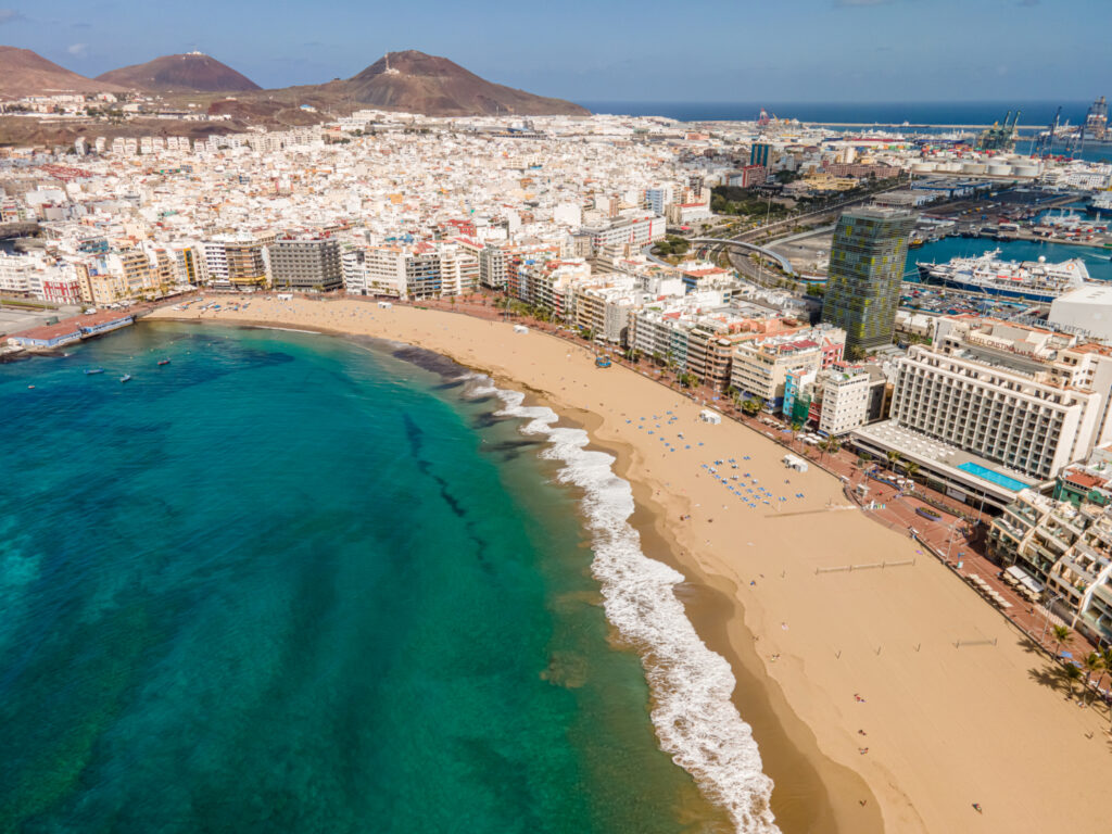 Aerial view of Las Palmas city with a beachfront, buildings, and clear blue waters.