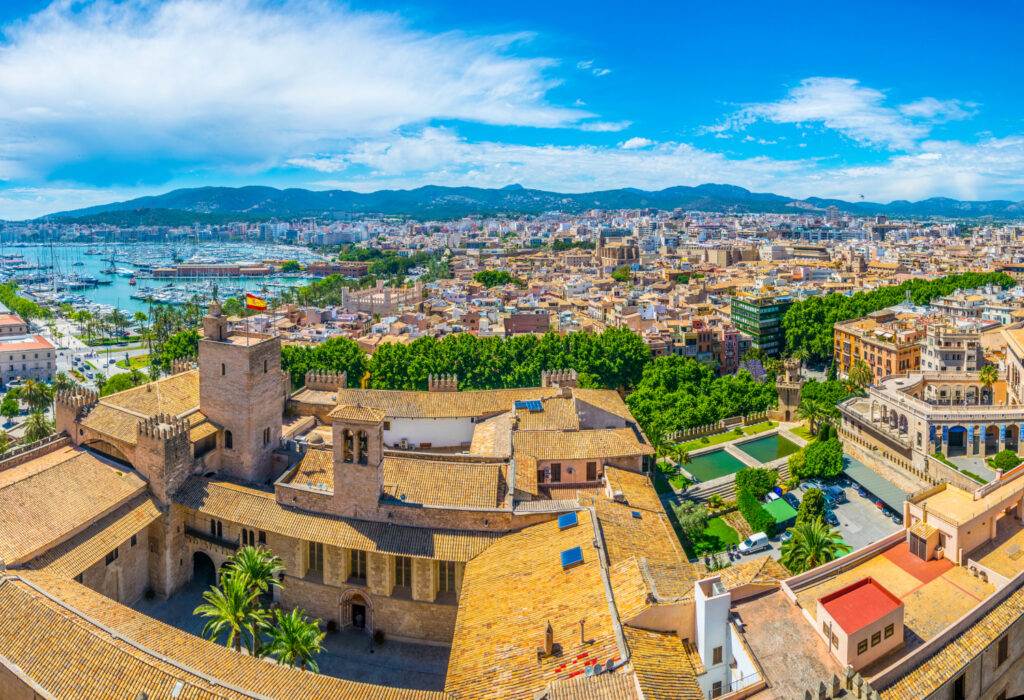 A panoramic view of Palma, showcasing the cityscape with buildings and water in the background under a clear blue sky.