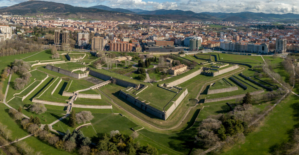 Aerial view of the fortified complex of the Citadel of Pamplona with green grassy areas and surrounding urban landscape under a cloudy sky.