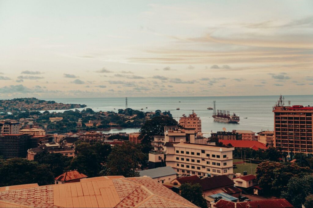 Aerial view of Freetown, Sierra Leone, at dusk with buildings in the foreground and the ocean in the background.