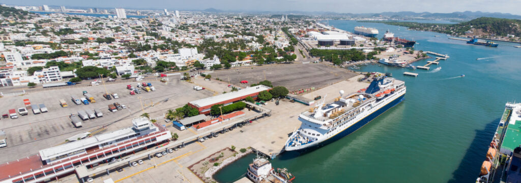 A panoramic view of a Sinaloa coastal area, showcasing a docked cruise ship, nearby infrastructure, and cityscape.