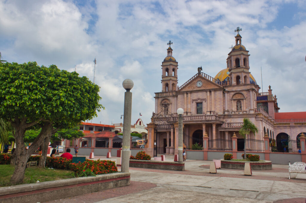 A colonial church with two towers and a dome, in a plaza with a bush and lamp post, possibly in Tabasco, Mexico.