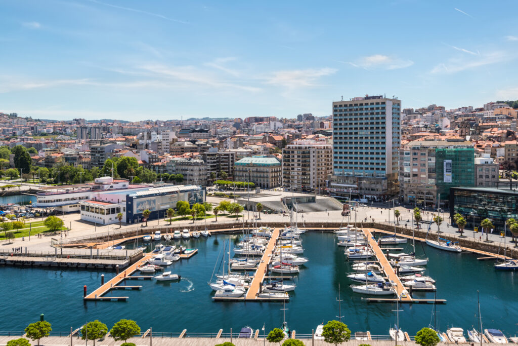 Aerial view of a marina with boats docked in Vigo, Spain, surrounded by buildings and a clear sky.