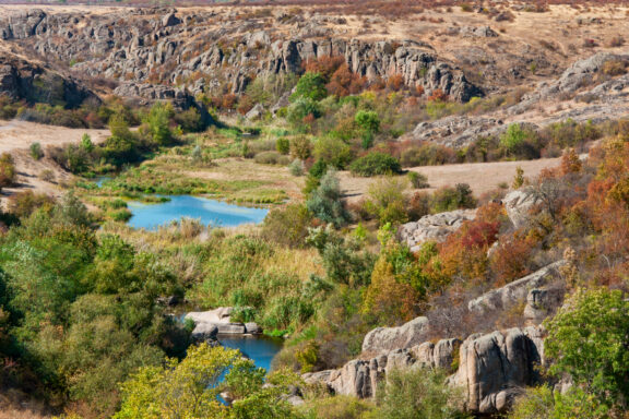 A scenic view of Aktov Canyon with rocky terrain and a small river running through green vegetation.