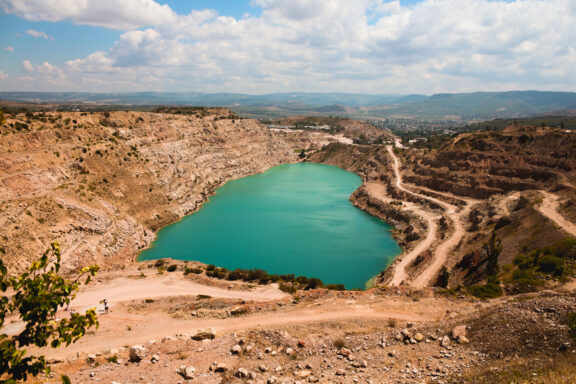 A scenic view of a turquoise lake nestled within a rugged quarry in Balaklava, Crimea, under a partly cloudy sky.