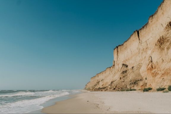 A sandy beach with a high, eroded cliff on one side under a clear blue sky, likely in Odessa.