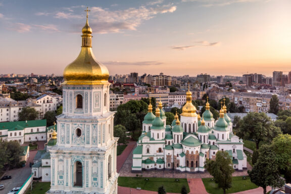 Aerial shot of a golden-domed bell tower in Kyiv, amidst buildings with green roofs at twilight.