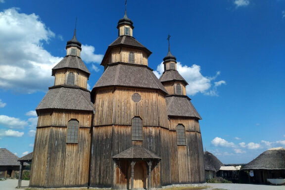 A traditional wooden church with multiple domes on Khortytsya Island under a clear blue sky.