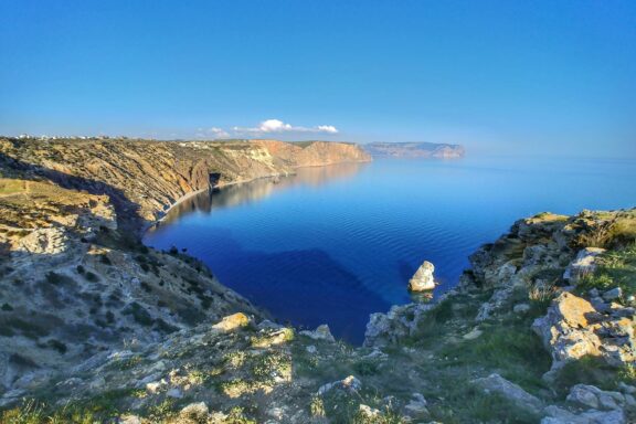 A coastal view of Crimea featuring a calm blue sea, clear sky, and rugged cliffs.