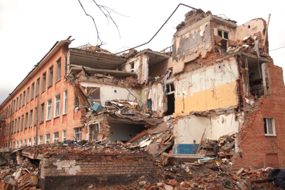 A damaged red brick school building with collapsed walls and debris in Chernihiv.