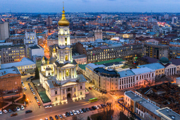 Aerial view of Kharkiv city at night with illuminated buildings and a prominent church with a golden dome.