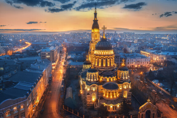 Aerial view of the illuminated Annunciation Cathedral in Kharkov during twilight with cityscape in the background.