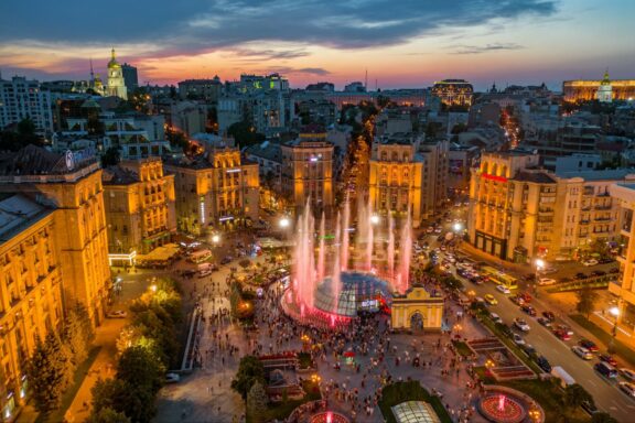 An image of a cityscape at dusk, featuring illuminated buildings and a fountain, likely in Kyiv.