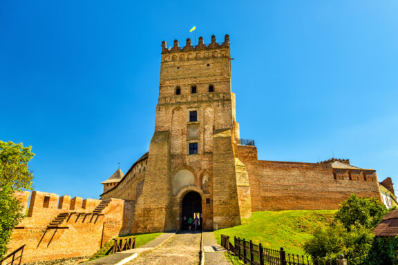 A medieval stone castle with a prominent central tower under a clear blue sky, located in Lubart's Castle, Ukraine.