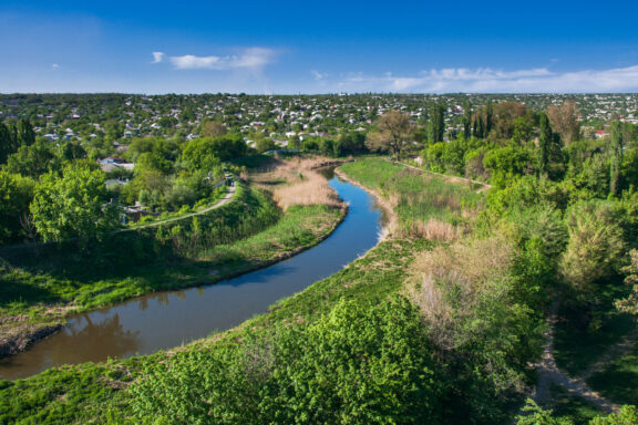 Aerial view of the Luhan River meandering through a lush landscape with trees and greenery on either side under a blue sky with scattered clouds.