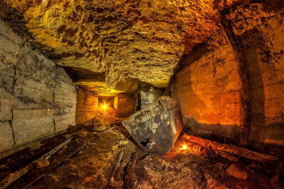 A dimly lit underground tunnel in the Odessa Catacombs with rough stone walls and a large, overturned, rusted metal object in the foreground.